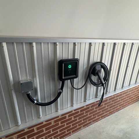 Level 2 EV charger and junction box mounted on a metal building wall with the connector holstered