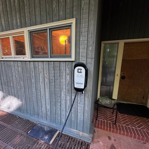 Wall-mounted Level 2 EV charger installed beside a covered entry, cable run down to the parking pad