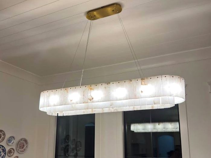 Linear glass chandelier installed over a dining table on a shiplap ceiling